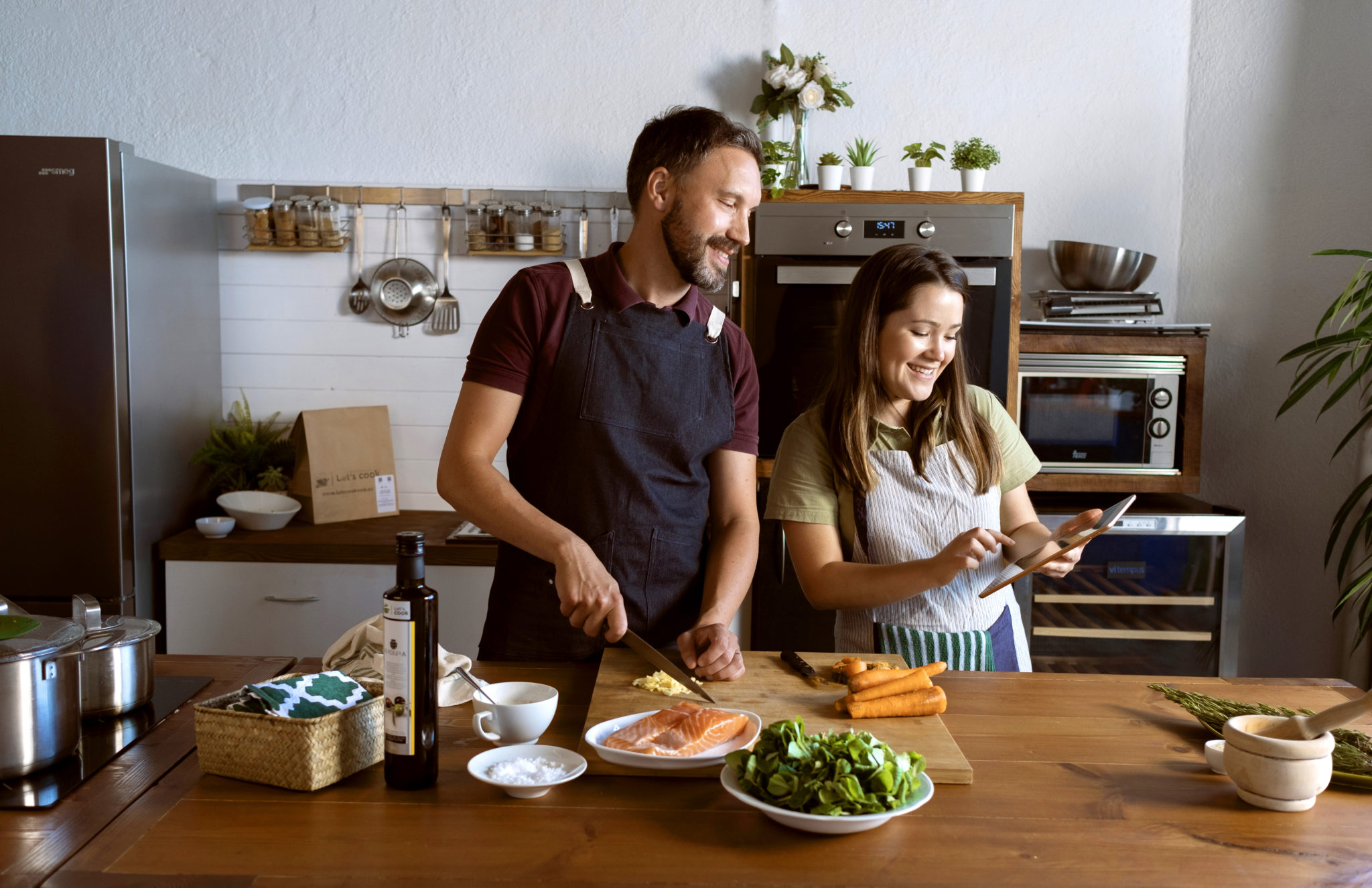 couple cooking in the kitchen together. Following a Lets cook recipe from their iPad